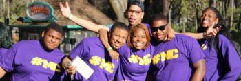 group in purple shirts smiling with a sign in the background