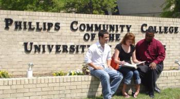 three people sitting by 'phillips community college of university' sign