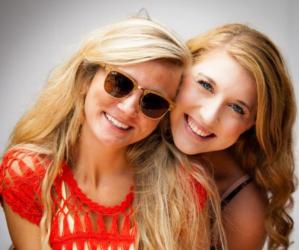 two smiling young women wearing sunglasses and casual attire