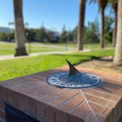 sundial on brick pedestal with palm trees in background