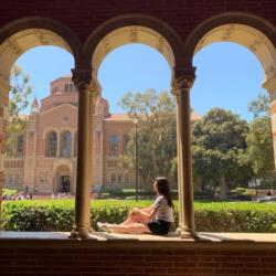 student sitting on campus with buildings in background