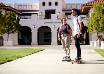 two students walking with a skateboard