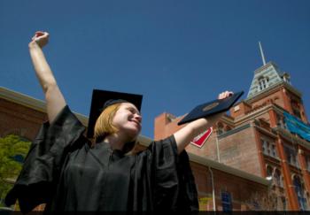 graduating student joyfully holding diploma in cap and gown