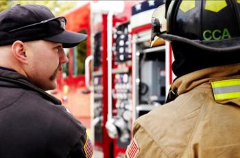 police officer and firefighter with 'CCA' on uniform in front of fire truck