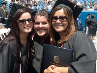 three graduates smiling with a diploma