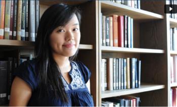 student by bookshelves looking at camera