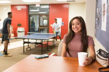 student with coffee smiling by ping pong table