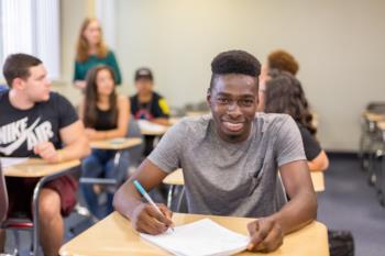 smiling student writing at desk in classroom