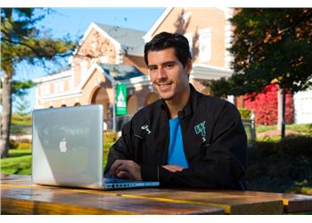 male student with laptop sitting outside on campus