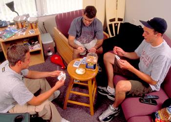 three students playing cards in a dorm room