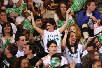 crowd of students cheering at an event with green pompoms