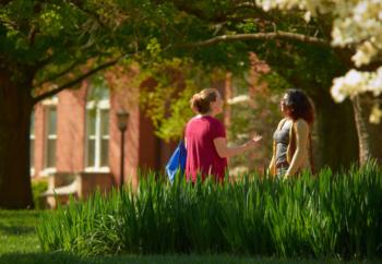 two people talking on a lush campus lawn