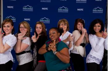 group of people posing with hand gestures in front of a backdrop with 'NGTC' logos