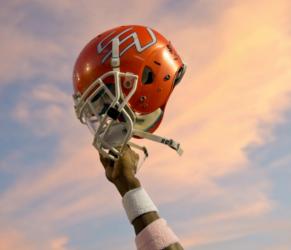 hand raising a football helmet against a sky background