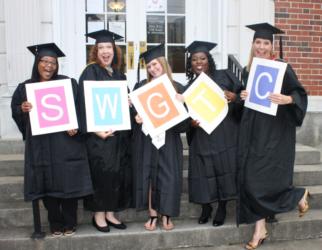 graduates holding signs with 'swgtc' letters in front of a building