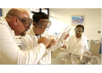 three people in lab coats examining a flask