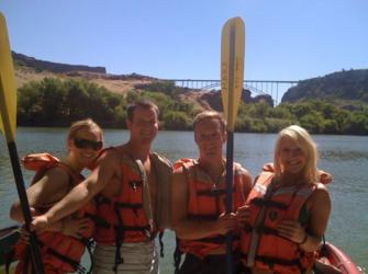 four people in life jackets with paddles near river