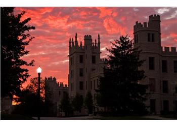 sunset behind a castle-like building with lit lamp post