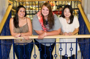 three smiling female students leaning on a railing