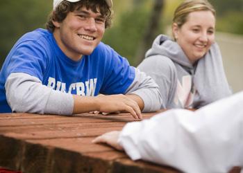 two students smiling, sitting at an outdoor table