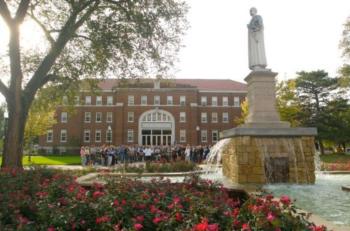 students gathered in front of campus building with statue and fountain