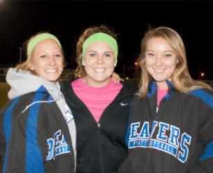 three women posing together at night, wearing sports attire