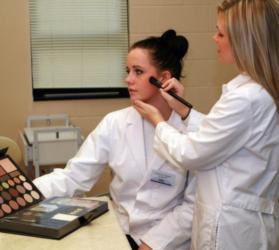 two students in lab coats practicing makeup application