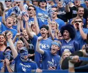 crowd of fans in blue with 'kentucky' shirts cheering at an event