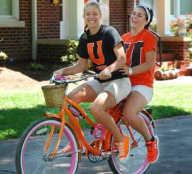 students riding tandem bicycle, laughing with 'U' shirts