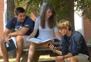 three students studying outdoors on a bench