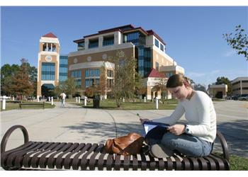 student studying outdoors with campus building in background