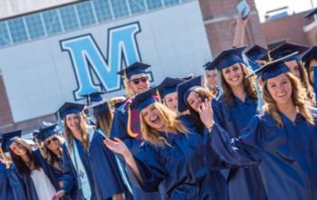 graduates in blue gowns with 'M' emblem in background