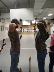 two people practicing archery indoors