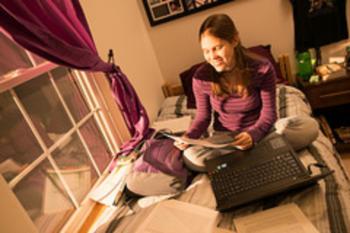 student studying on a bed with laptop and books