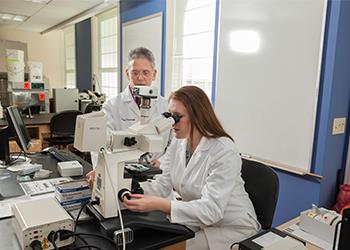 professor and student using microscope in lab