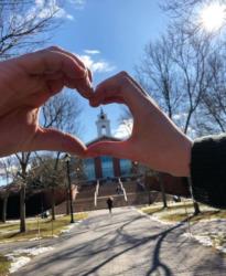 hands forming a heart shape with a university tower in the background