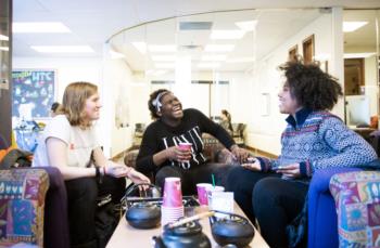 three students laughing and talking on a couch