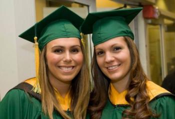 two graduates smiling in green caps and gowns