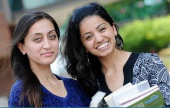 two smiling students holding books outdoors