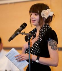 woman speaking at mic with papers and flower in her hair