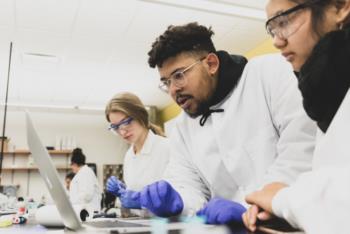 students in lab coats working on a laptop