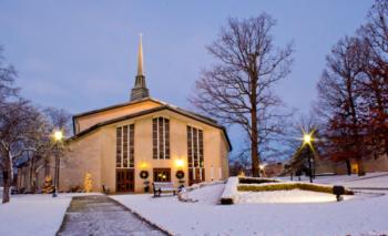 twilight view of campus chapel with snow and lit lamps