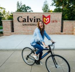 student cycling past 'Calvin University' sign