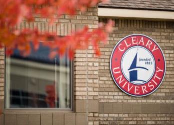 cleary university logo on brick wall with window and foliage