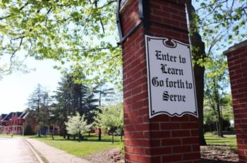 sign: 'Enter to Learn, Go forth to Serve' with campus backdrop