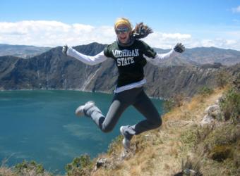 person mid-jump with 'michigan state' sweater by a lake