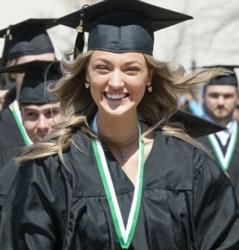 smiling graduate in cap and gown with peers in background