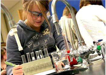 student conducting a lab experiment wearing 'academy' hoodie