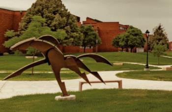 sculpture in a grassy campus area with buildings in the background