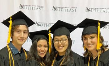 four graduates smiling in caps and gowns